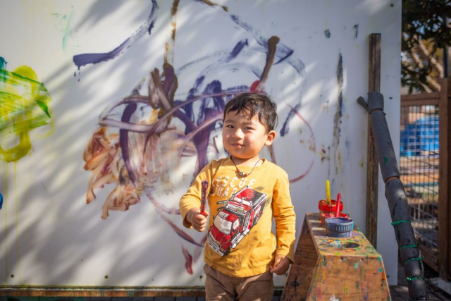 Child painting with huge strokes of the paintbrush on the paint wall