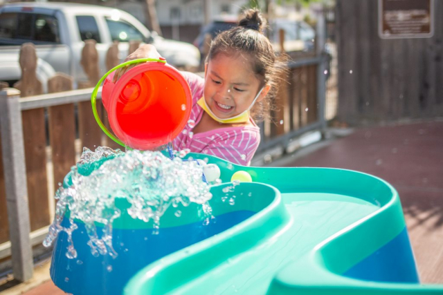 Child poiuring water to move toys down a ramp